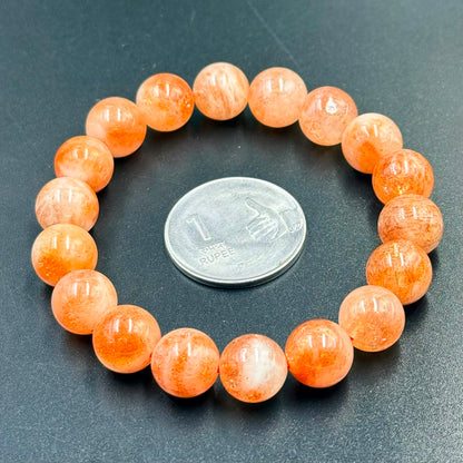 Sunstone Bracelet with round orange beads arranged in a circle around a 1 rupee coin on black background