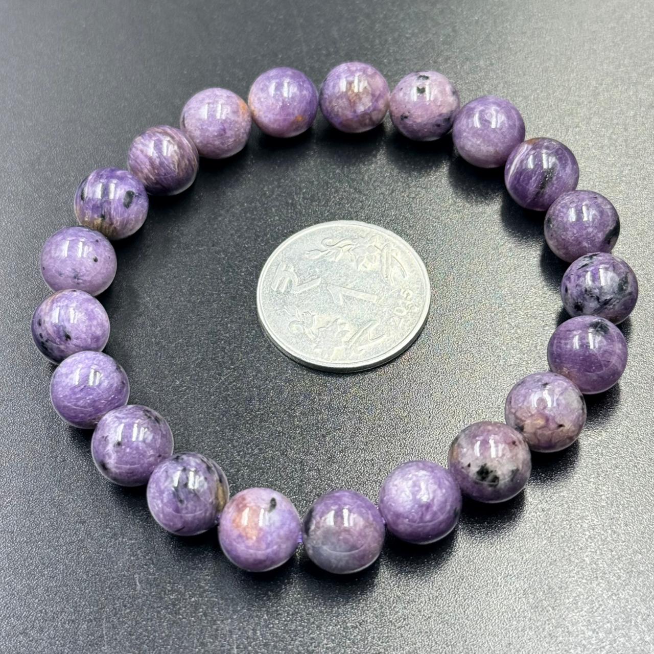 Charoite Bracelet with round polished purple beads and a coin for size reference on black surface