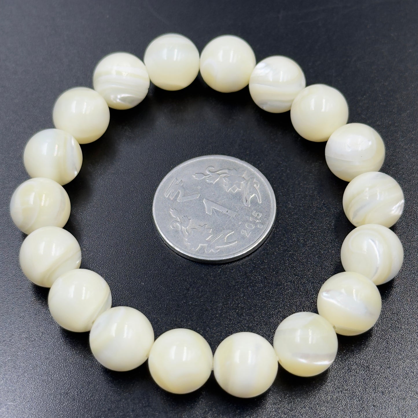 Mother of Pearl Bracelet with round beads arranged in a circle around a coin on black surface
