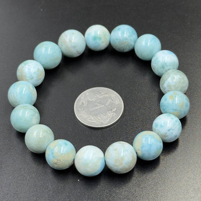 Larimar Bracelet with round light blue beads encircling a silver coin on a black background