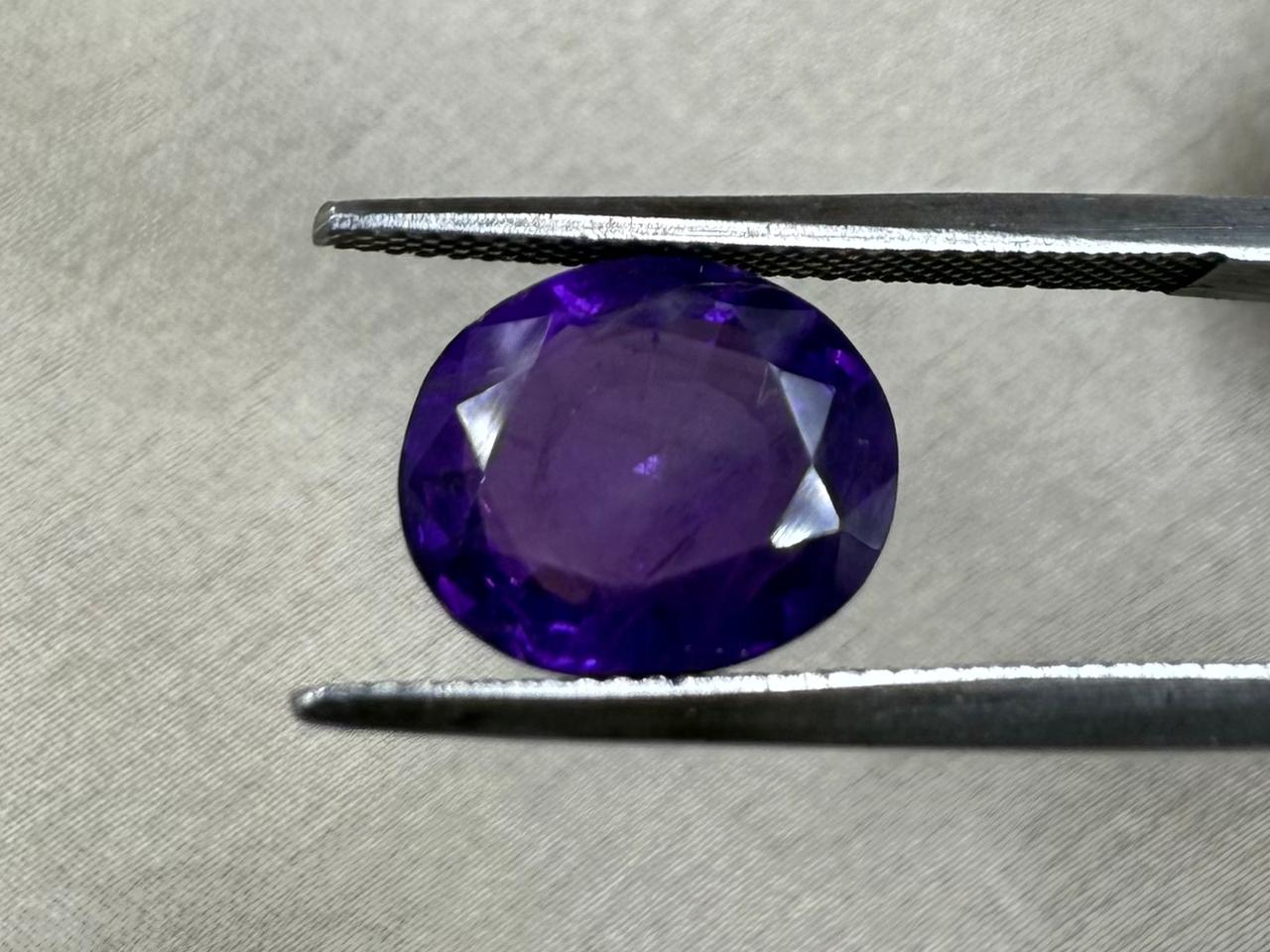 Purple gemstone held by tweezers on a textured gray background