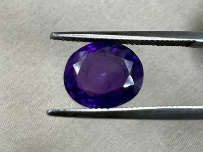 Purple gemstone held by tweezers on a textured gray background