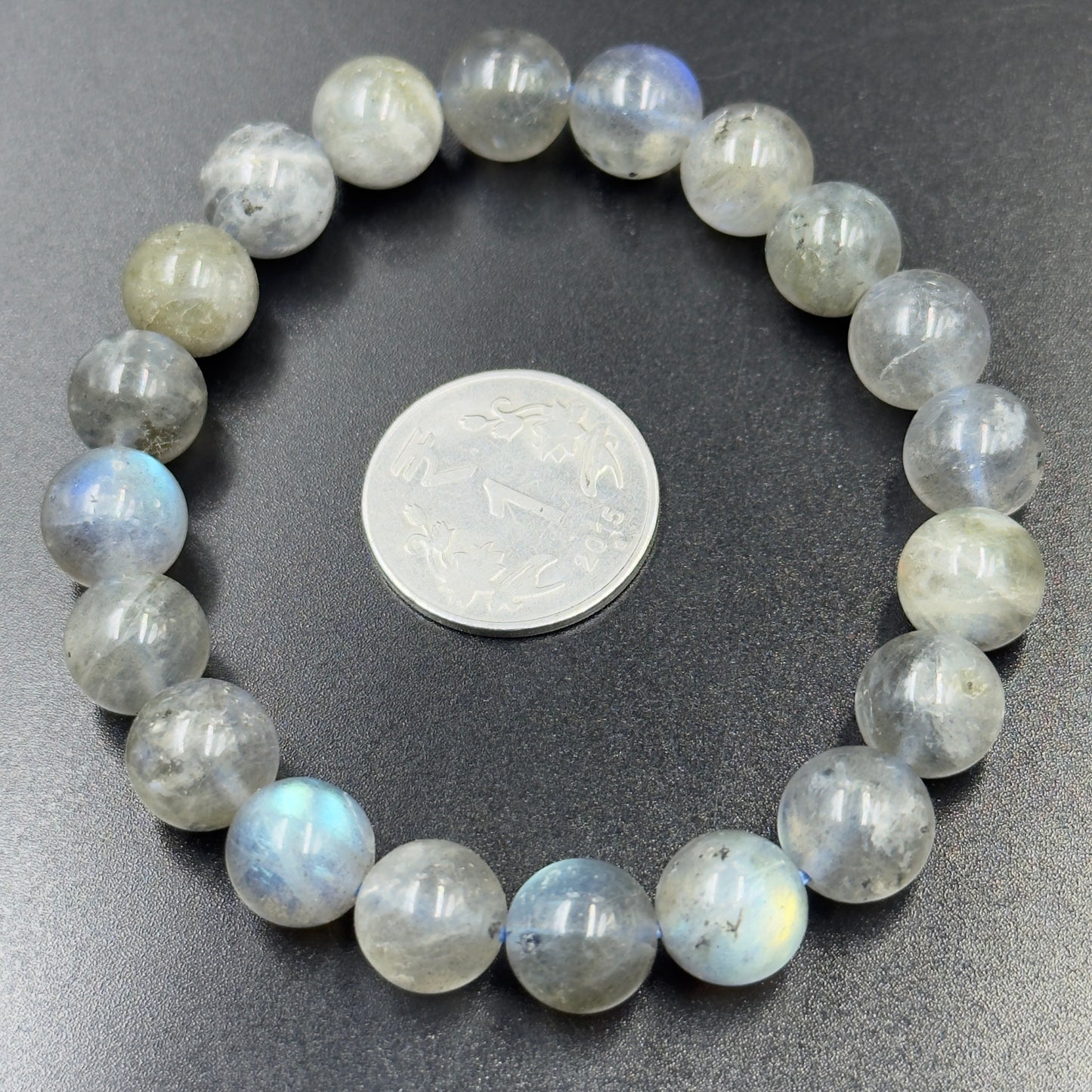 Labradorite bracelet with round translucent beads showing blue and yellow flashes, next to a coin for scale.