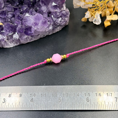 Rose Quartz Rakhi Thread Bracelet with a pink faceted bead and two gold beads on a pink thread next to a ruler and amethys...