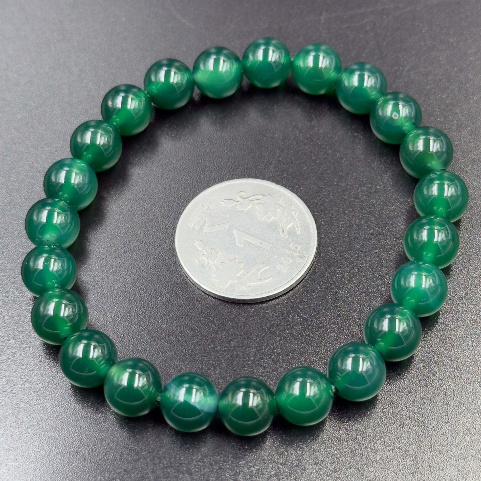 Green Onyx Bracelet with round glossy green beads arranged in a circle next to a silver coin on dark surface