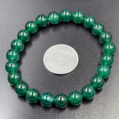 Green Onyx Bracelet with round glossy green beads arranged in a circle next to a silver coin on dark surface