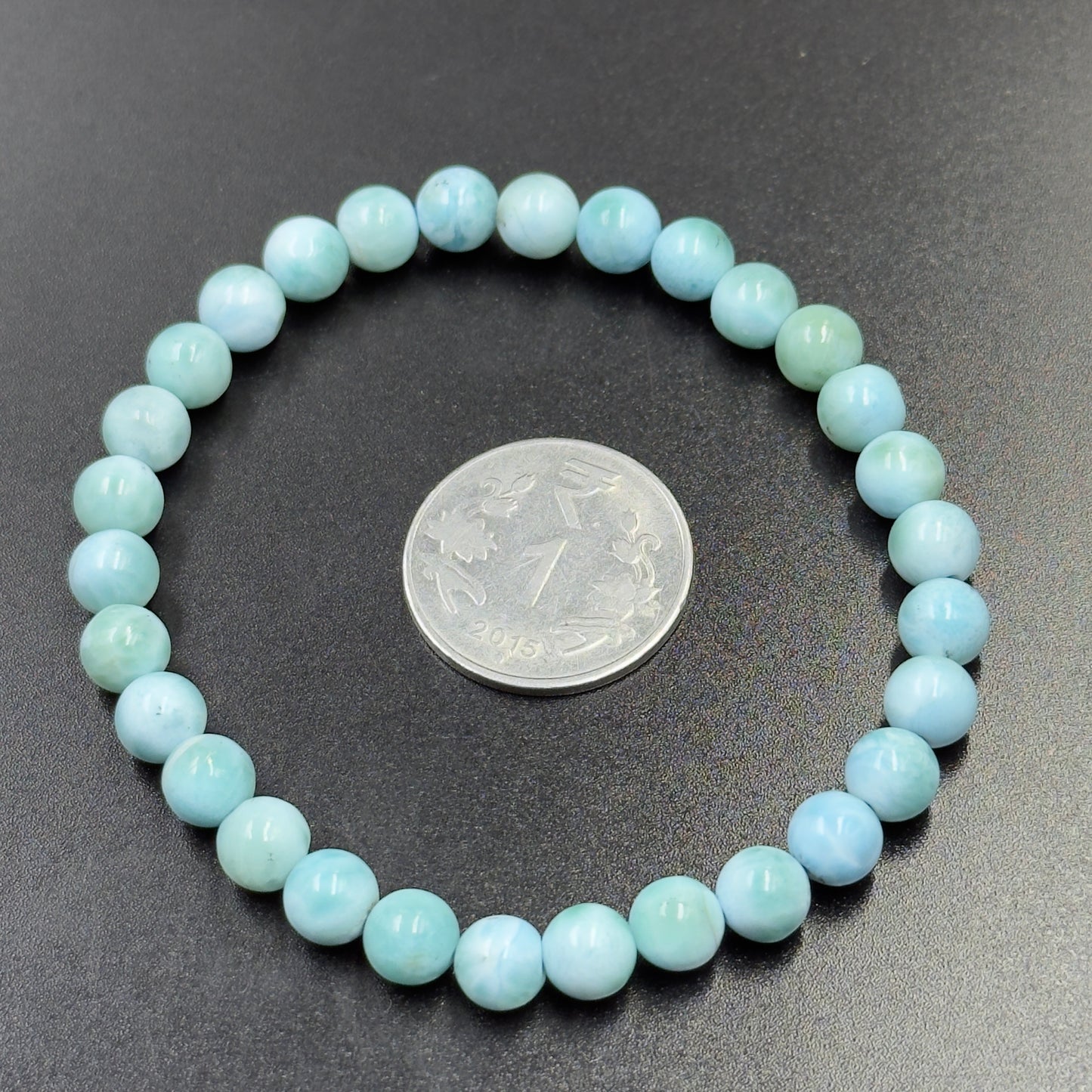 Larimar Bracelet with round light blue beads encircling a 1 rupee coin on black surface