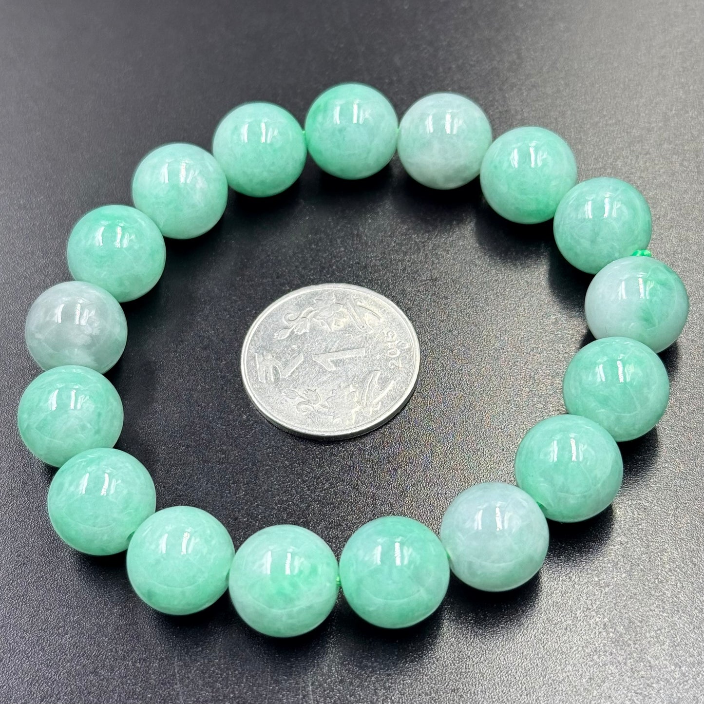 Jadeite Jade bracelet with round apple green beads arranged in a circle on black surface