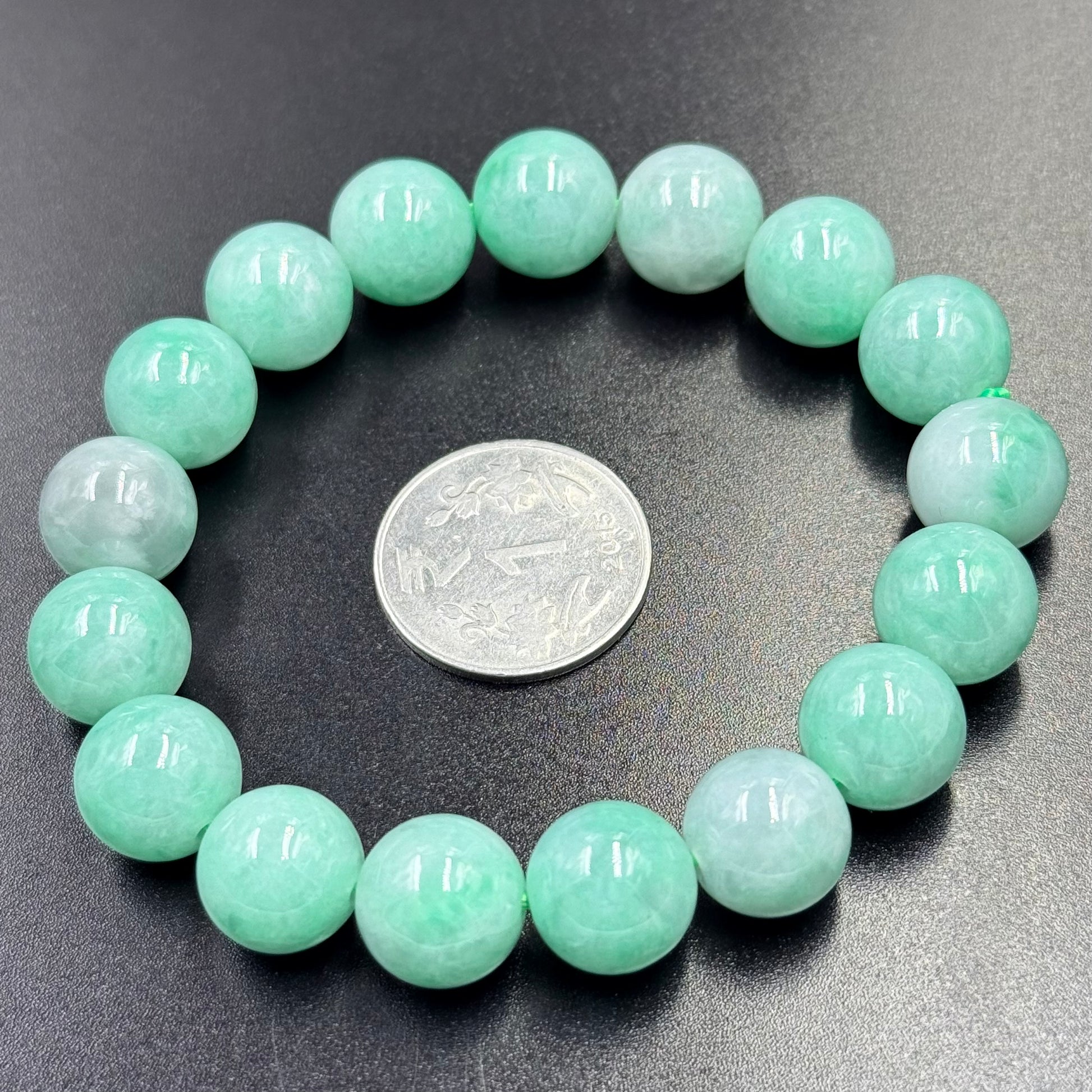 Jadeite Jade bracelet with round apple green beads arranged in a circle on black surface
