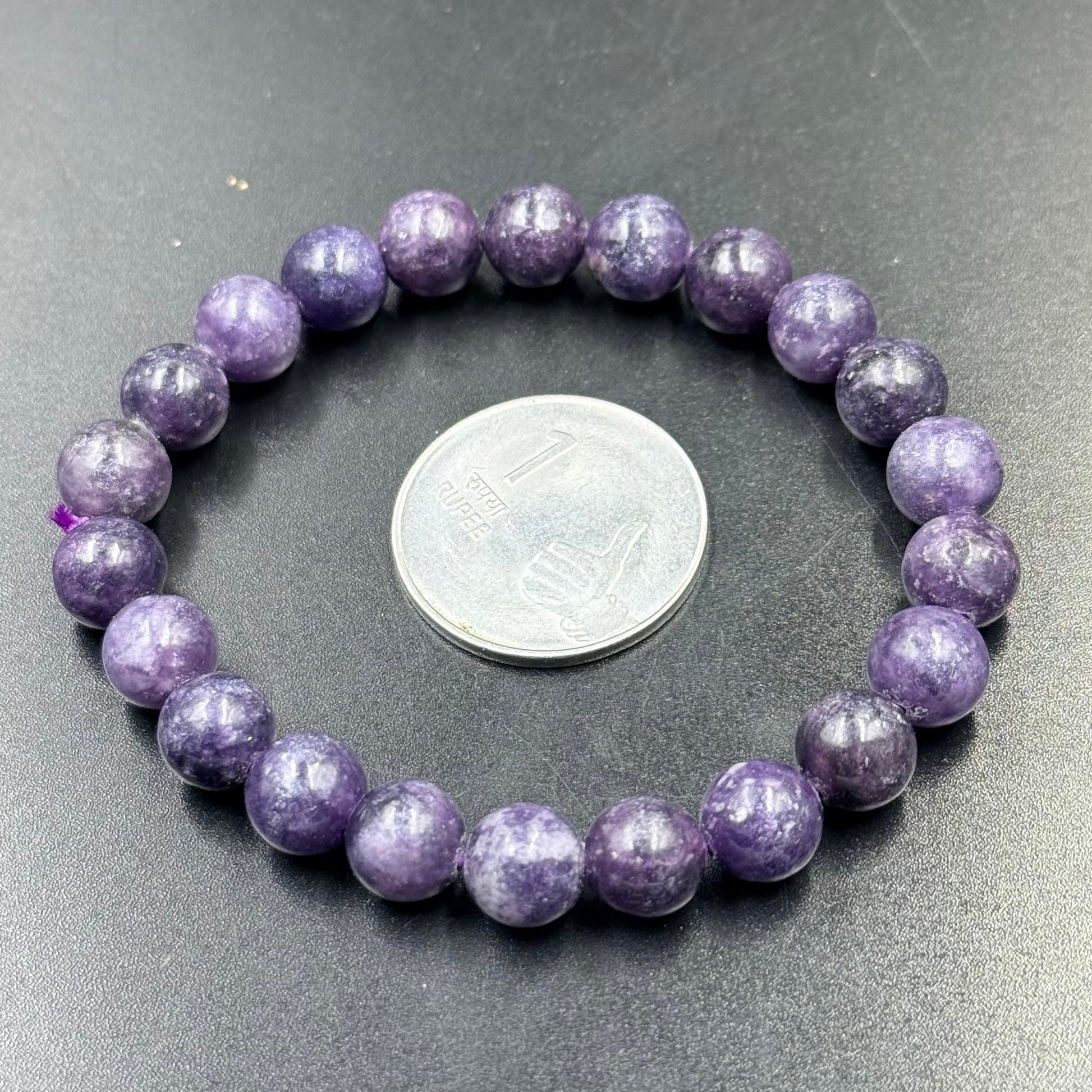 Charoite Bracelet with purple beads arranged in a circle around an Indian one rupee coin on black surface