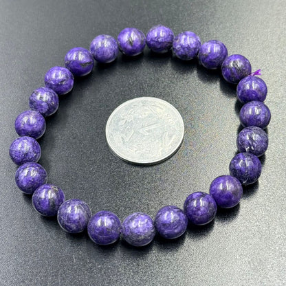 Charoite Bracelet with round purple beads arranged in a circle around a coin on black surface