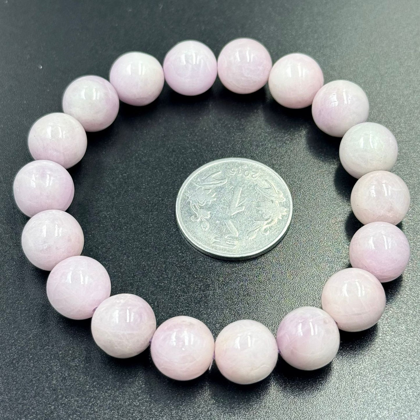 Pink Kunzite Bracelet with round polished beads arranged in a circle next to a coin on black surface