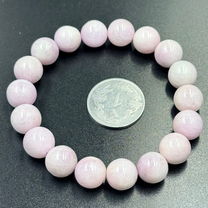 Pink Kunzite Bracelet with round polished beads arranged in a circle next to a coin on black surface