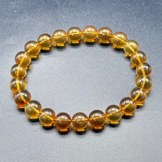 Amber bracelet made of round yellowish-brown beads laid out on gray textured background