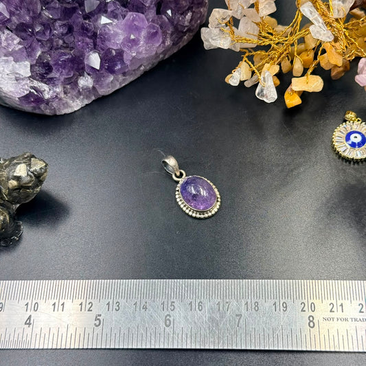 Amethyst oval locket pendant in 925 silver with scalloped bezel on dark background and ruler