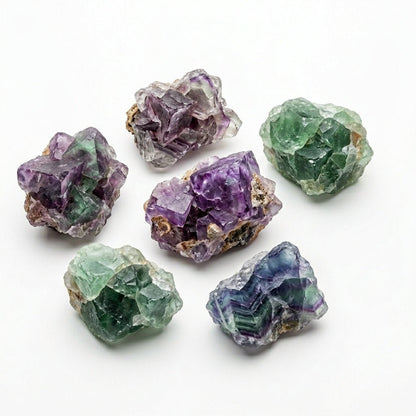 Assorted raw natural fluorite crystal pieces showing purple, green, and blue tones on white