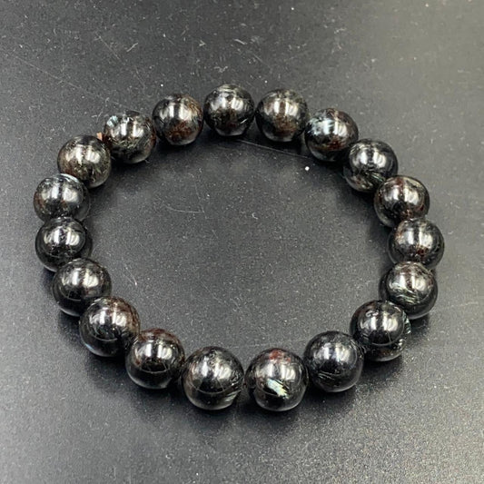 Astrophyllite bracelet close-up of round dark beads with metallic shine on gray surface