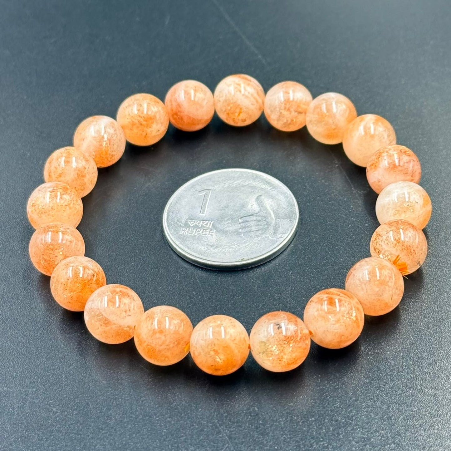 Sunstone Bracelet with round orange beads arranged in a circle around a 1 rupee coin on black surface