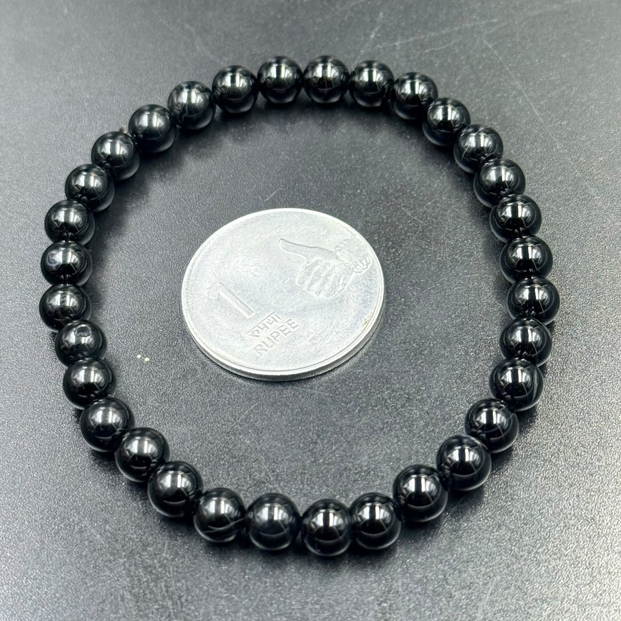 Black obsidian 6mm bracelet close-up with coin for scale on gray surface