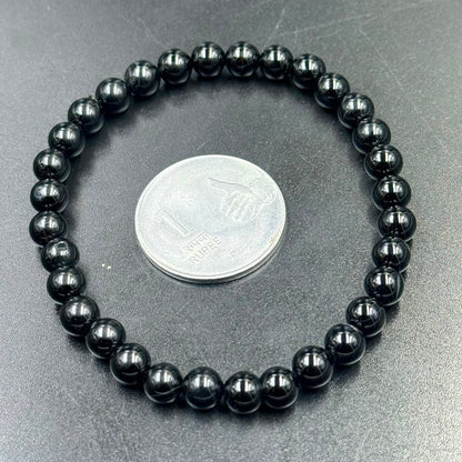 Black obsidian 6mm bracelet close-up with coin for scale on gray surface