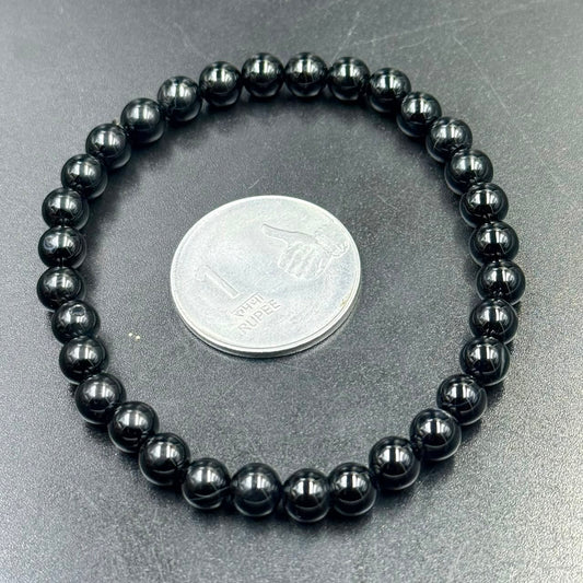 Black obsidian 6mm bracelet close-up with coin for scale on gray surface
