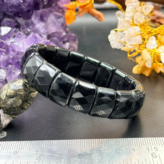 Black onyx faceted square bead bracelet with gold-tone clasp, close-up on tabletop
