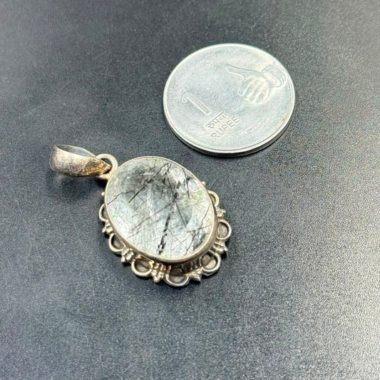 Black rutilated quartz locket pendant set in 925 silver on dark textured background