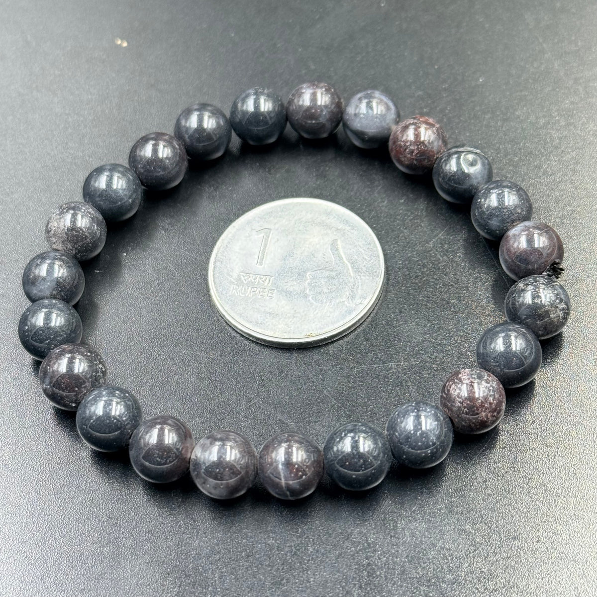 Close-up of bloodstone jasper beaded bracelet on gray surface with coin for size reference