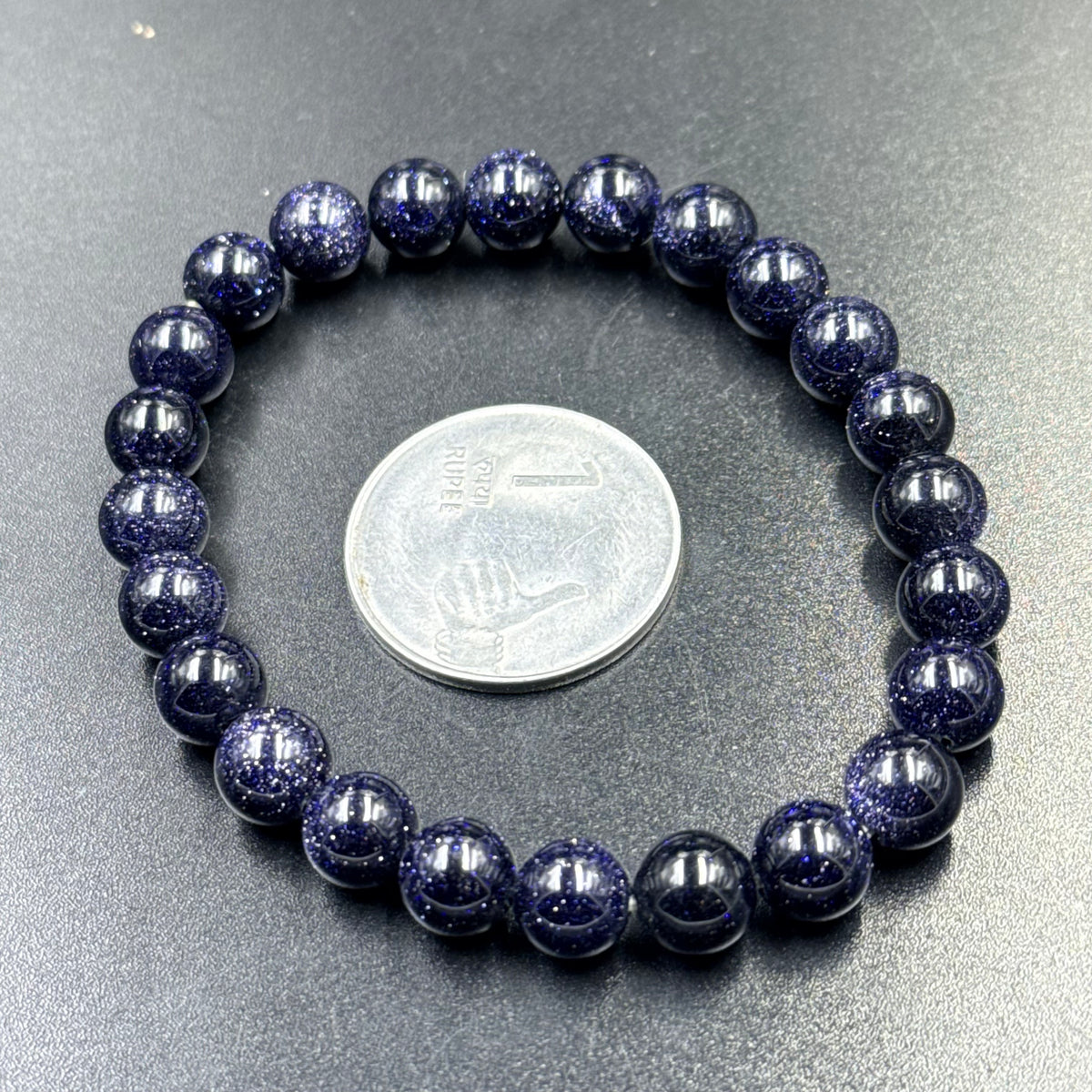 Close-up of blue goldstone beaded bracelet with coin for scale on gray background