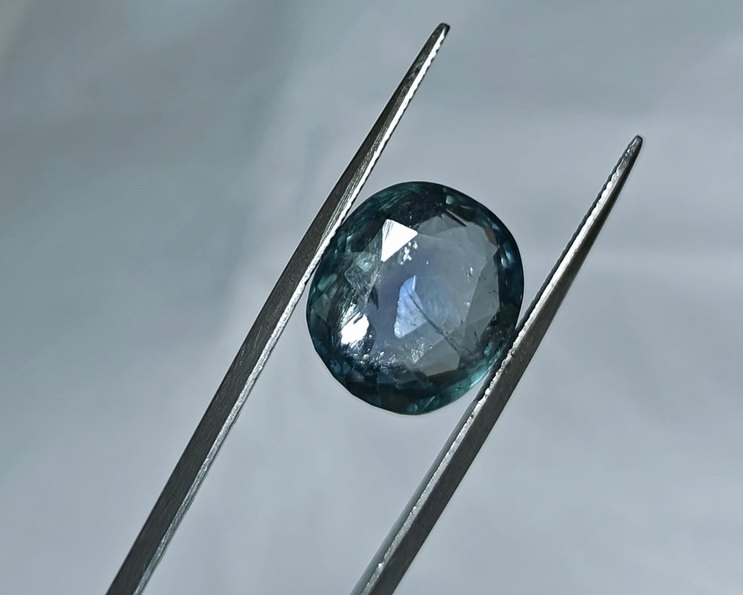 Faceted gemstone held between tweezers against a neutral background