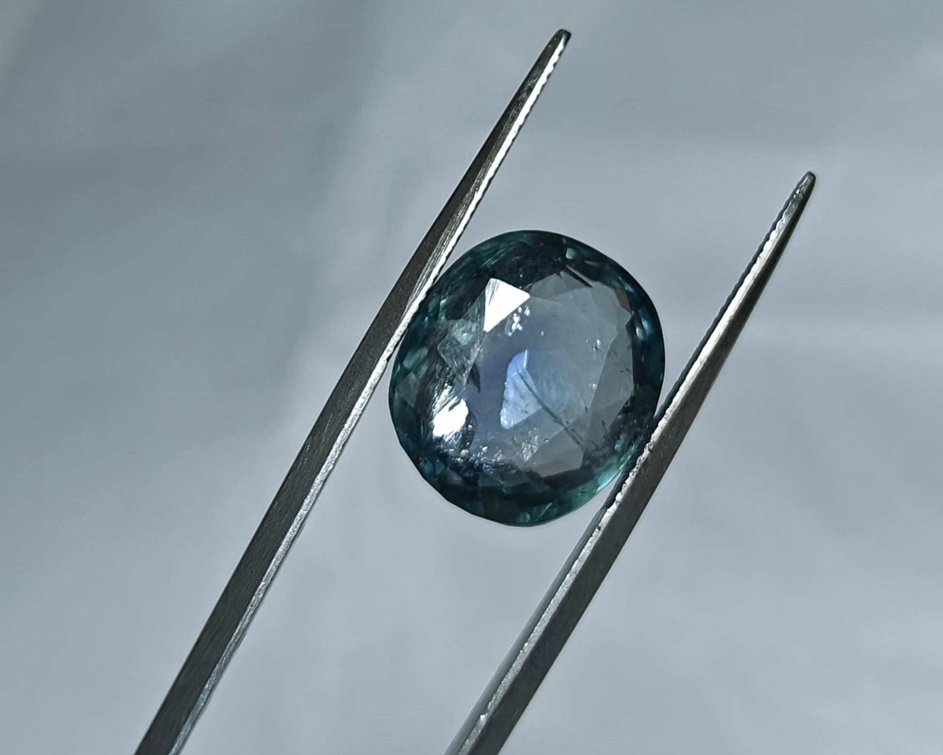 Faceted gemstone held between tweezers against a neutral background