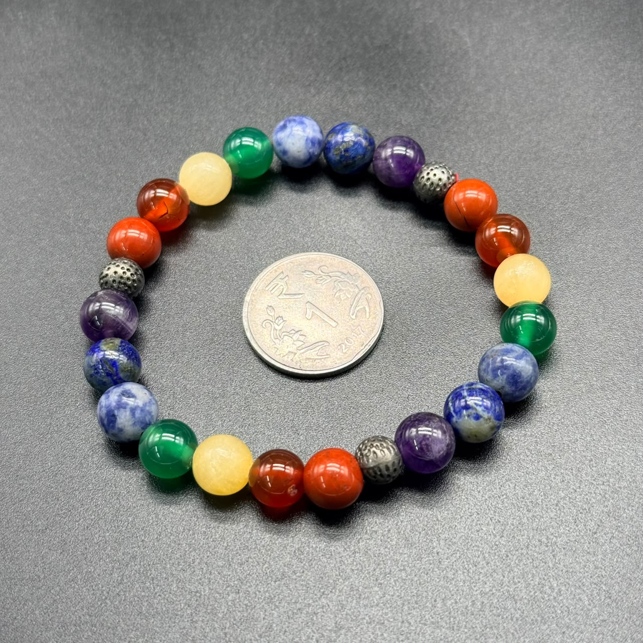 7 Chakra Balance Bracelet with multicolored round beads and silver textured spacer beads next to coin
