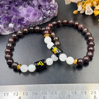 Capricorn zodiac bracelet laid on dark stone with garnet and milky quartz beads and black charm