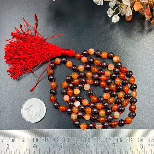 Carnelian and garnet jaap mala beads with red tassel laid on dark background and measuring scale