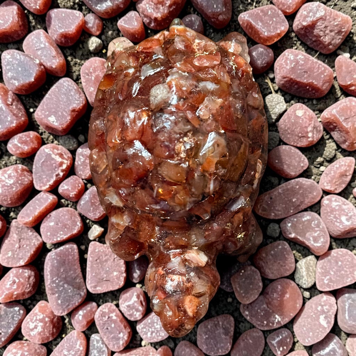 Carved carnelian turtle figurine on dark pebbles with pink stones around it
