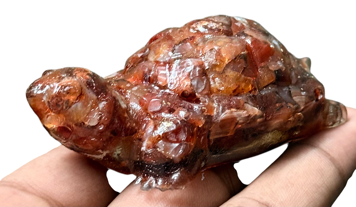 Carved carnelian turtle figurine held in hand showing glossy orange-brown detail