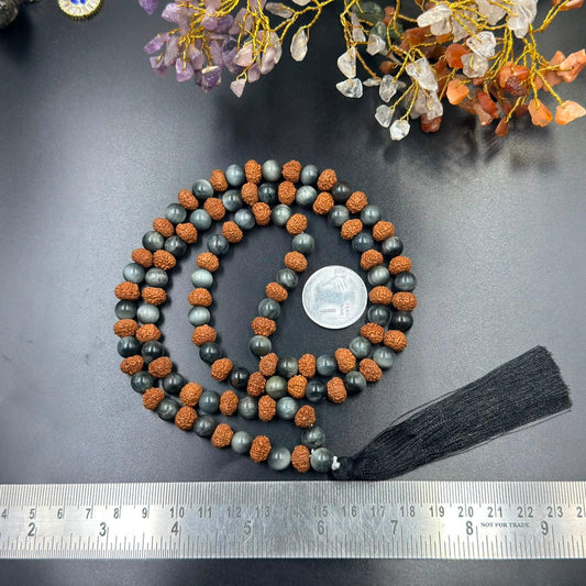 Jaap mala close-up laid out on dark fabric, showing grey cat’s eye beads and textured rudraksha beads