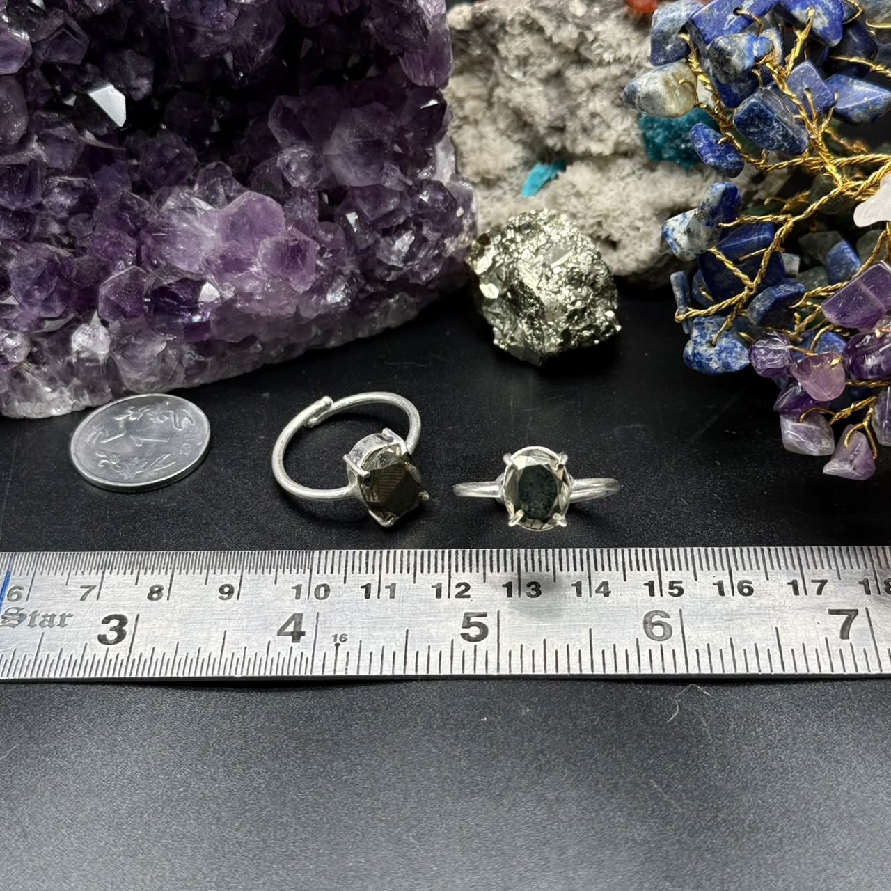 Two Natural Pyrite Rings (Adjustable) placed on black surface with a ruler, amethyst and mineral stones nearby.