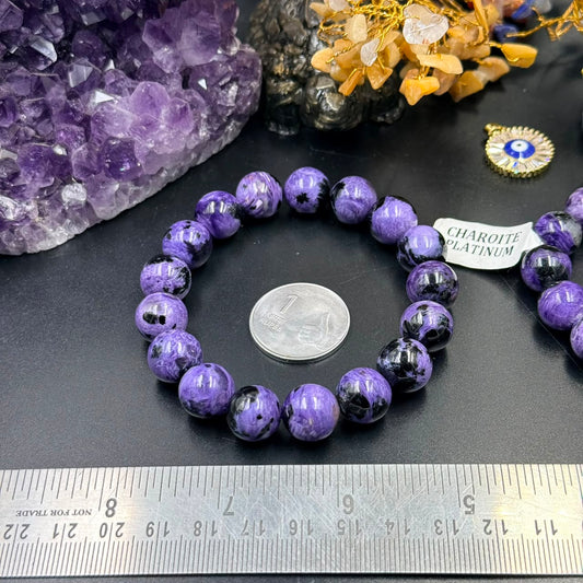Charoite bead bracelet with coin and label card on dark stone background