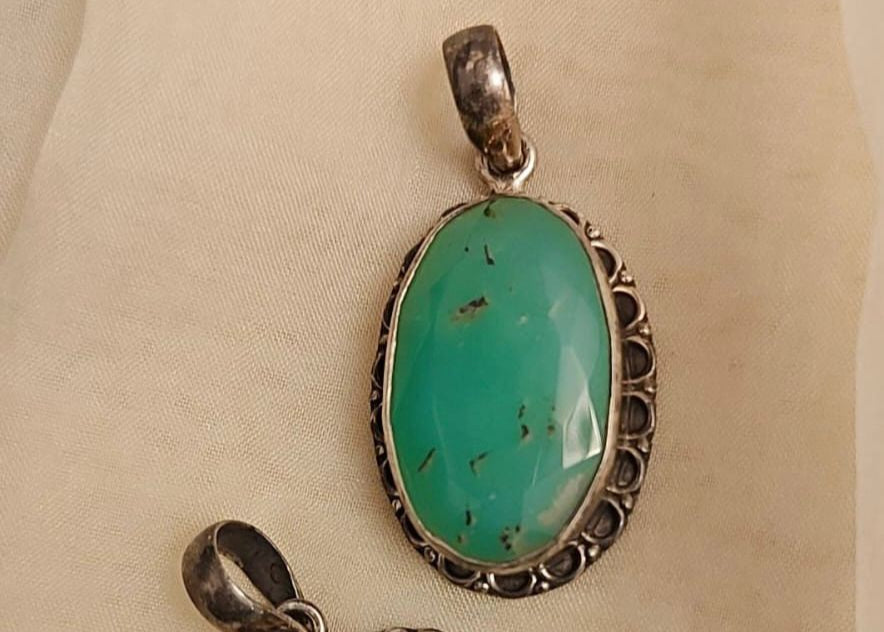 Two green stone pendants with silver settings on a beige background