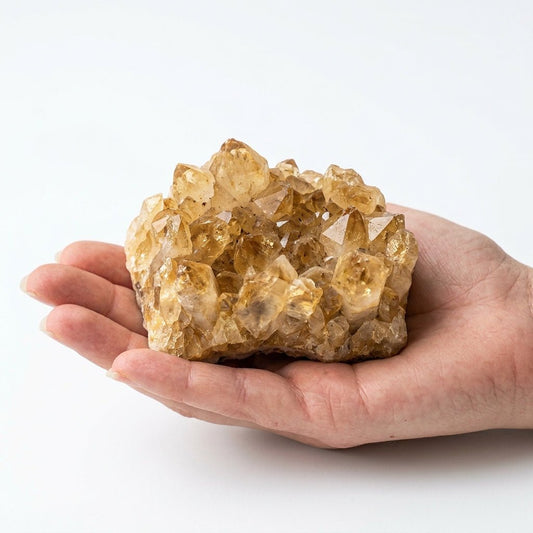 Raw citrine crystal cluster held in an open hand, natural yellow quartz on white