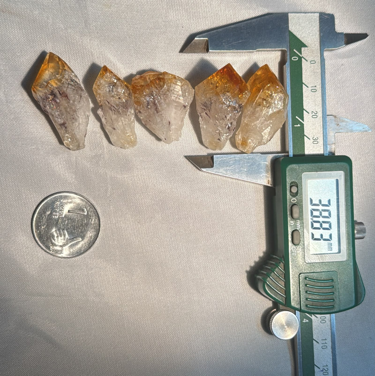 Five Citrine Rough Pointers arranged on white cloth with digital caliper and a coin nearby