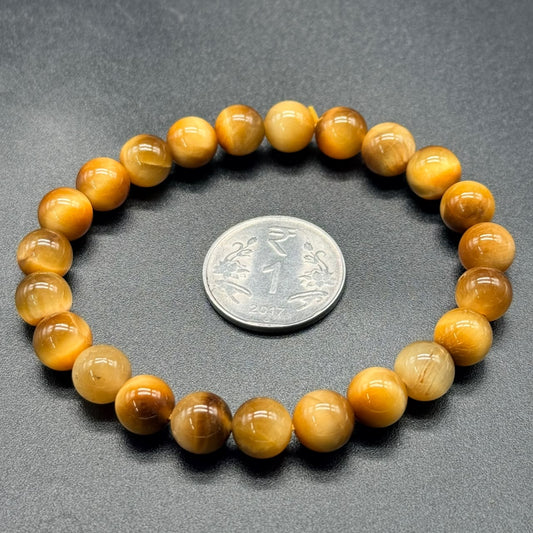 Close-up of tiger’s eye cat’s eye bracelet beads next to a coin for scale
