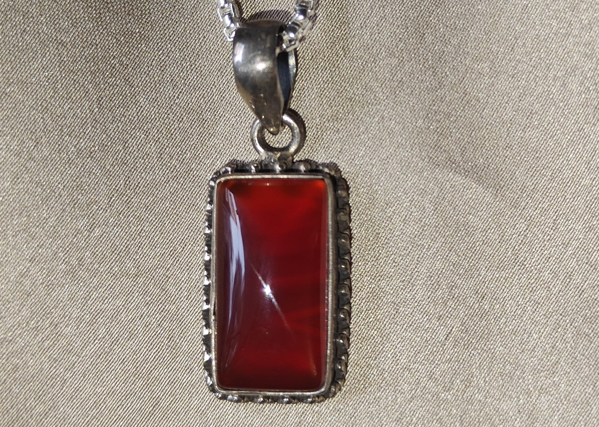 Silver necklace with a red pendant on a beige fabric background