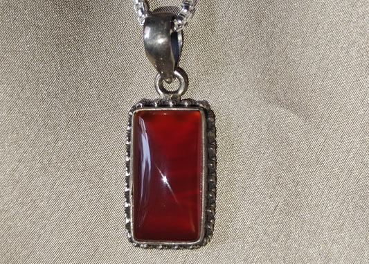 Silver necklace with a red pendant on a beige fabric background