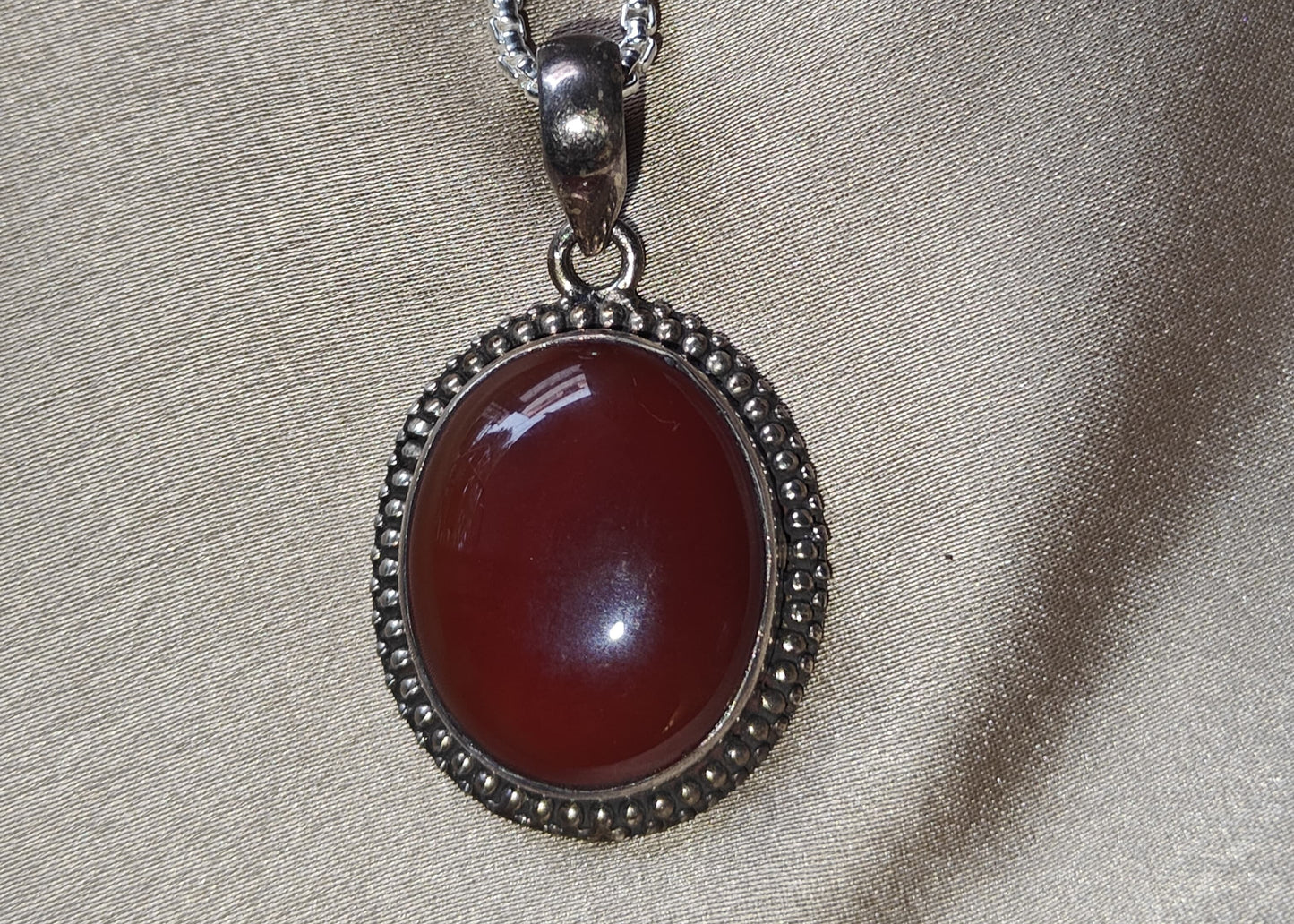 Necklace with a red pendant on a beige fabric background.