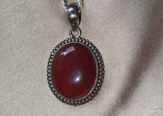 Necklace with a red pendant on a beige fabric background.