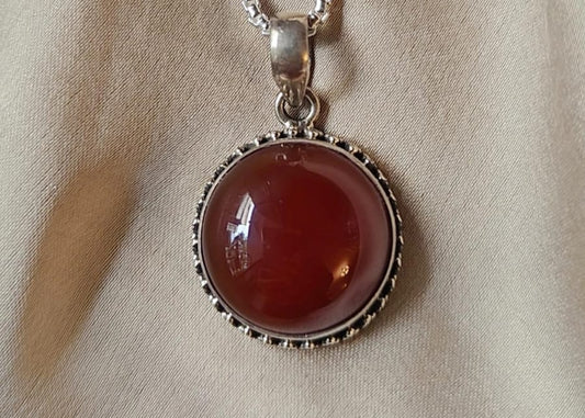Carnelian stone pendant on a silver chain against a beige fabric background
