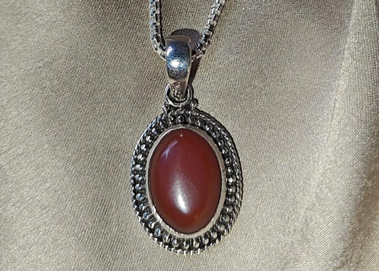 Silver necklace with a red stone pendant on a beige fabric background.
