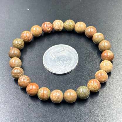 Color Cobble bracelet of round multicolor beads shown beside a large coin on dark fabric